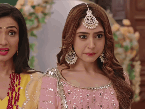 a woman wearing a pink dress and earrings stands next to another woman in a yellow dress