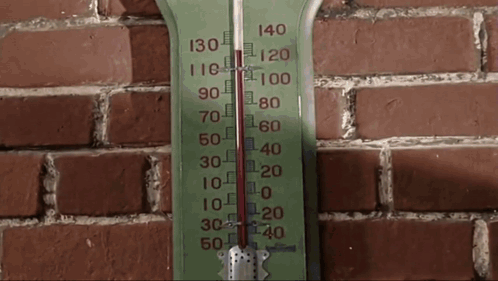 a green thermometer hanging on a brick wall shows the temperature at 130