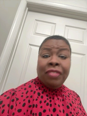a woman in a red and black polka dot shirt is standing in front of a white door making a funny face .