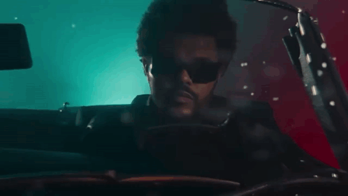 a man wearing sunglasses is driving a red car .