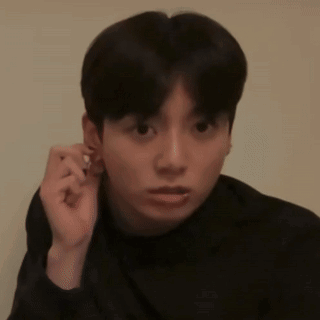 A man touches his ear and looks off-camera with a puzzled expression.