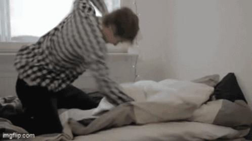A person repeatedly punches a pillow on a bed in frustration.