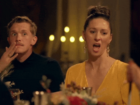 a man and a woman are sitting at a table and the woman is wearing a yellow dress and earrings .