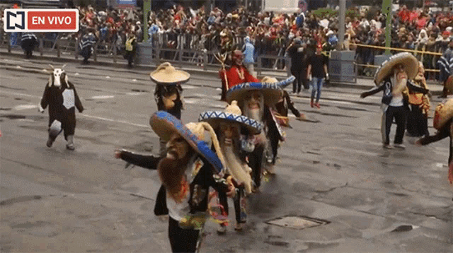 a group of people wearing sombrero hats are walking down a street in front of a crowd with a sign that says en vivo