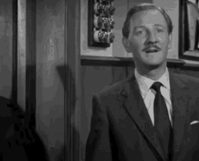 a man in a suit and tie is standing in a room in front of a wall .