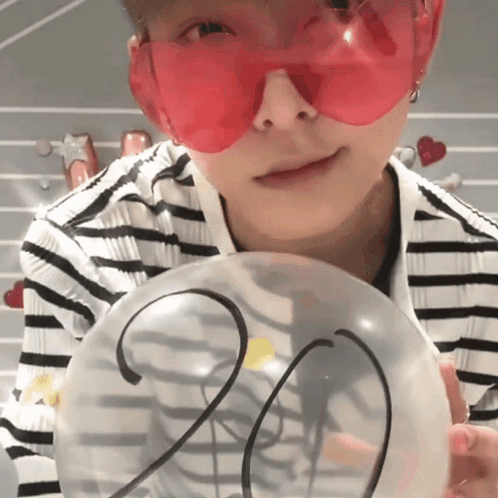 a person wearing red sunglasses is holding a clear balloon with the number 20 on it