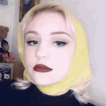 a woman wearing a yellow scarf around her head and red lipstick is making a funny face .