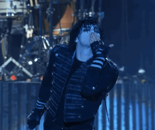 a man in a black jacket is singing into a microphone while wearing striped gloves