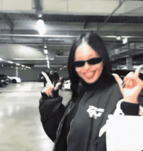 a woman wearing sunglasses and a black jacket is making a devil horns sign