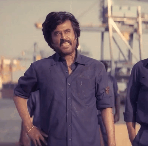 a man with a mustache and a blue shirt stands with his hands on his hips
