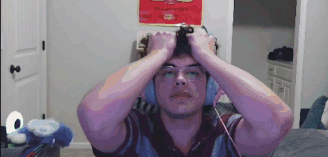 a man wearing headphones and glasses is holding his head in his hands .