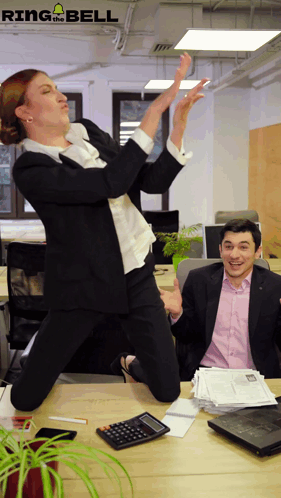 A person in an office jumps and dances on a desk as coworkers look on.