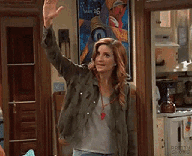A woman in a kitchen raises her hand for a self high five.