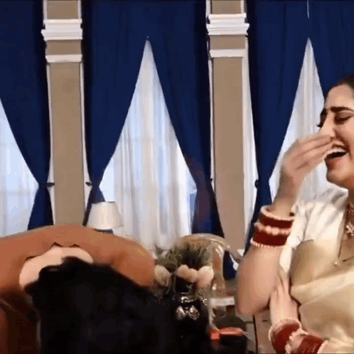 a woman is laughing while sitting on a couch in a room with blue curtains .