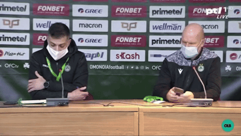 two men wearing face masks are sitting at a table in front of a wall that says fonbet
