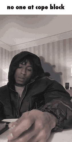a man in a hooded jacket is sitting at a table with the words no one at cope block above him