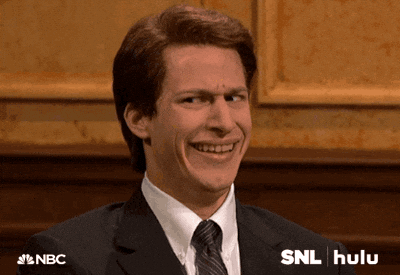 A smiling man gives an awkward, uncertain grin on an SNL set.