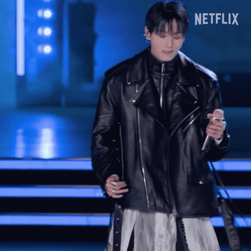 A performer in a long black leather coat dances on a blue-lit stage.