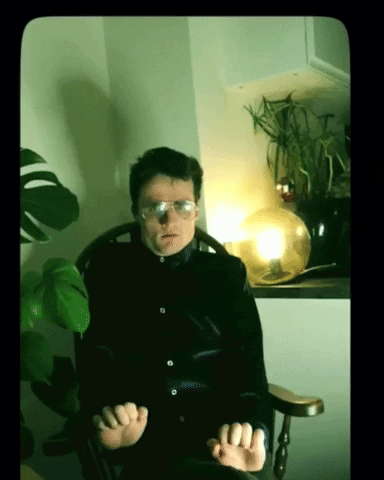 A person sits in a green-lit room with clenched fists, appearing tense.
