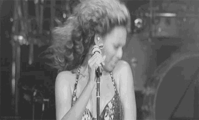 a woman is singing into a microphone on stage in a black and white photo .