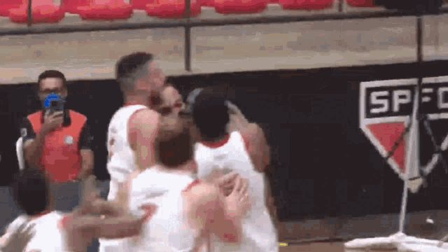 a group of basketball players are hugging each other in front of a wall with the word spfc on it