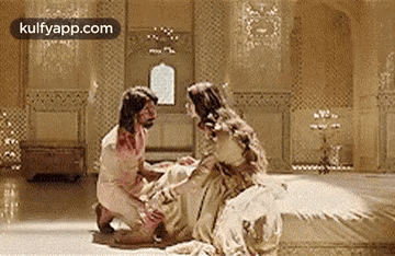 a man is kneeling down next to a woman sitting on a bed in a room .