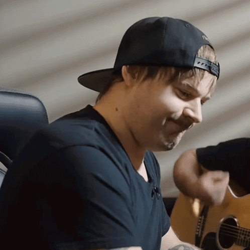 a man wearing a hat and a black shirt playing a guitar