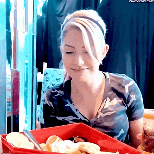 a woman is sitting at a table with a tray of food in front of her that says thenextbigthing on it