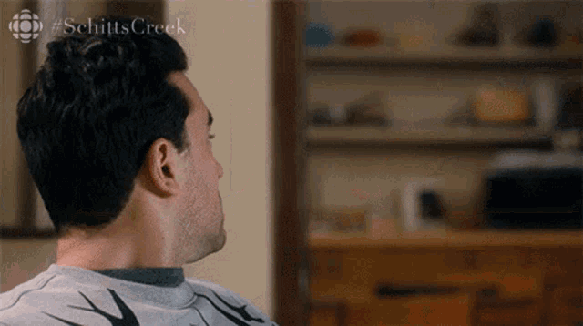 A man sits turned away in a room, looking downcast.