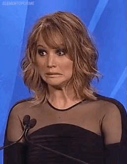 A woman at a podium makes an uncomfortable wide-eyed expression.