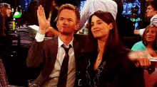 A dressed-up pair celebrate with raised hands in a crowd.