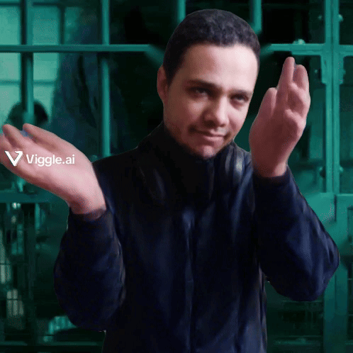 A man in dark clothing claps with one hand raised in a green-lit room.