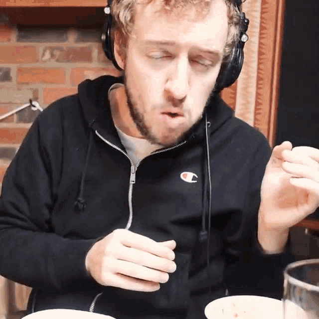 a man wearing headphones and a champion sweatshirt is eating food
