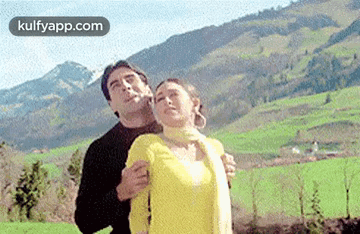 a man is hugging a woman in front of a mountain range .