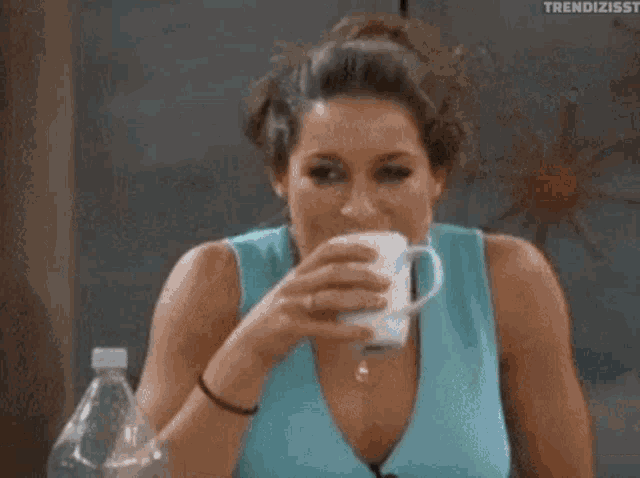 A woman drinks from a cup while holding back laughter.