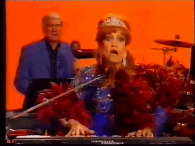 a woman is singing into a microphone while playing a keyboard in front of an orange background