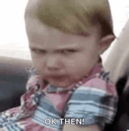 A frowning toddler looks intensely toward the camera with “OK THEN!” text.