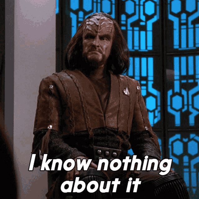 a man with a beard and long hair is sitting in front of a window and says i know nothing about it