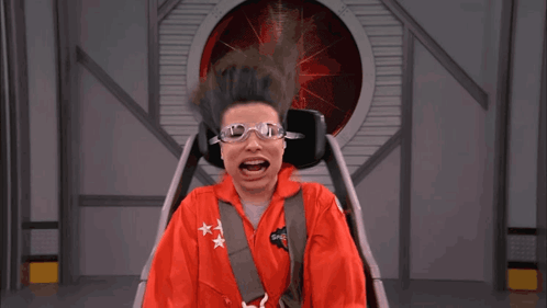 a woman wearing a red space suit and goggles is sitting in a chair with her mouth open
