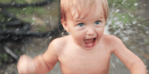 A wet baby splashes in water with an eager smile.