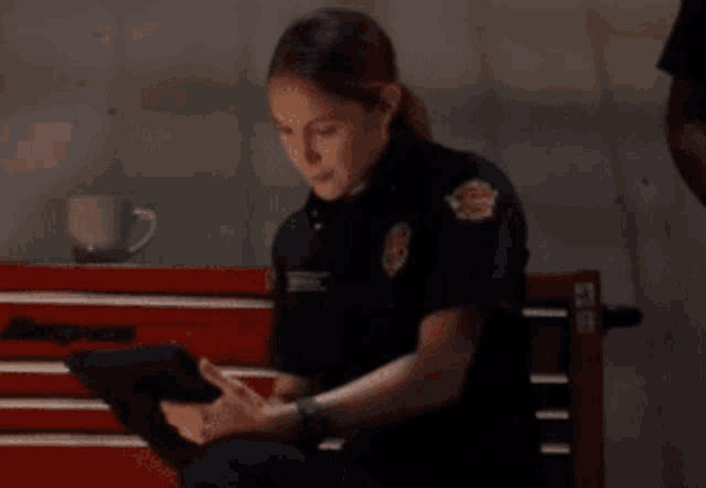 a woman in a firefighter uniform is sitting on a bench using a tablet