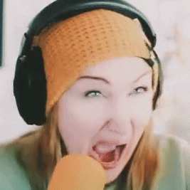 a woman wearing headphones and an orange beanie eating a carrot