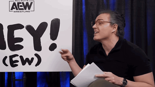 RJ City points while holding papers in front of the “HEY! (EW)” sign.