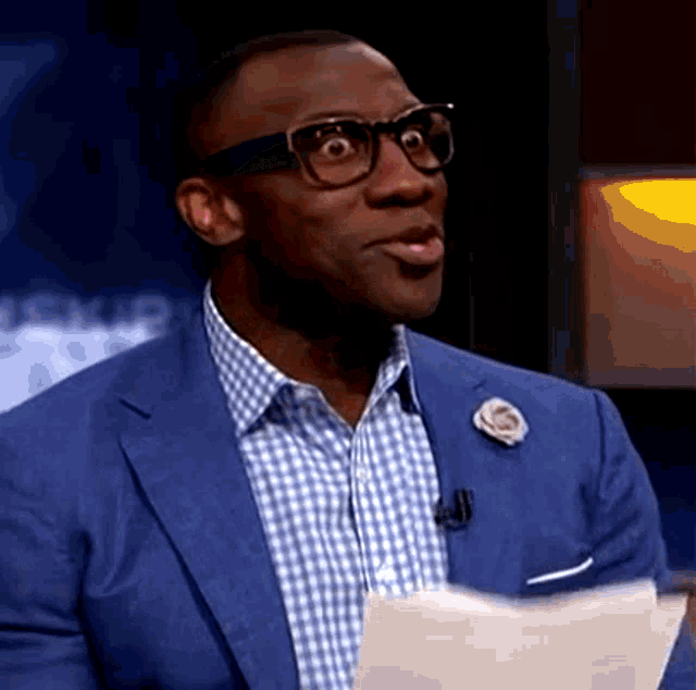 a man wearing glasses and a blue suit is holding a piece of paper in his hand .