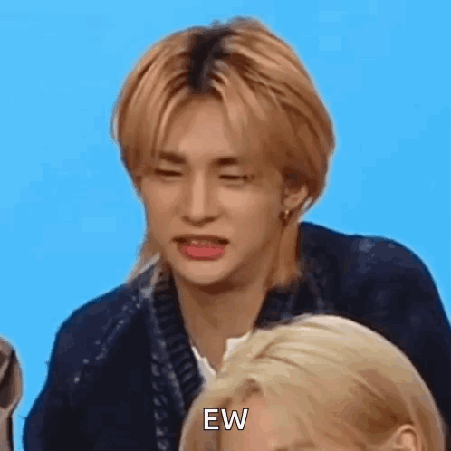 Hyunjin scrunches his face in visible disgust against a blue background.
