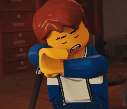 a lego figure is covering his mouth with his elbow while sitting on a chair