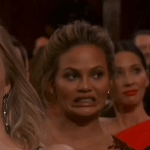 A woman makes an intensely uncomfortable grimace in a crowded room.