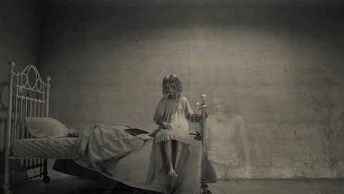 a little girl in a white dress stands in front of a bed