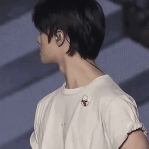 a man wearing ear buds and a white t-shirt has a pin on his shoulder