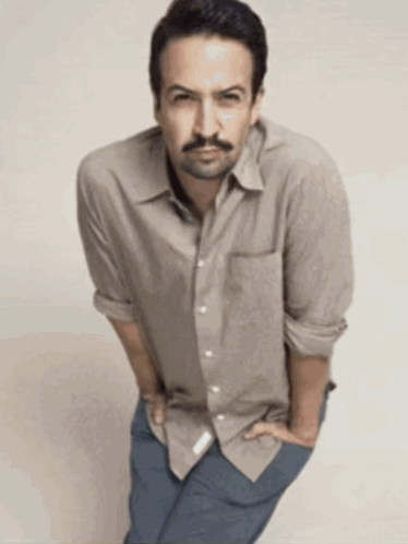 a man with a beard wearing a tan shirt and blue jeans